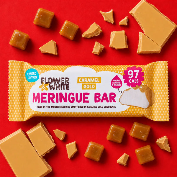 Flower White Caramel Gold Meringue Bar chocolate wrapped in a yellow patterned package, arranged on a bright red background with broken caramel pieces around it.