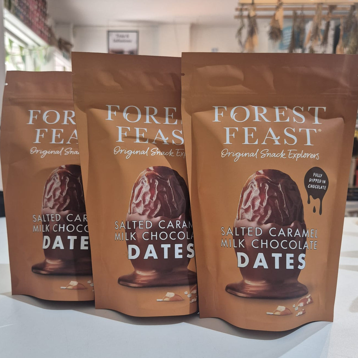 Three packages of Forest Feast salted caramel milk chocolate dates on a white surface.
