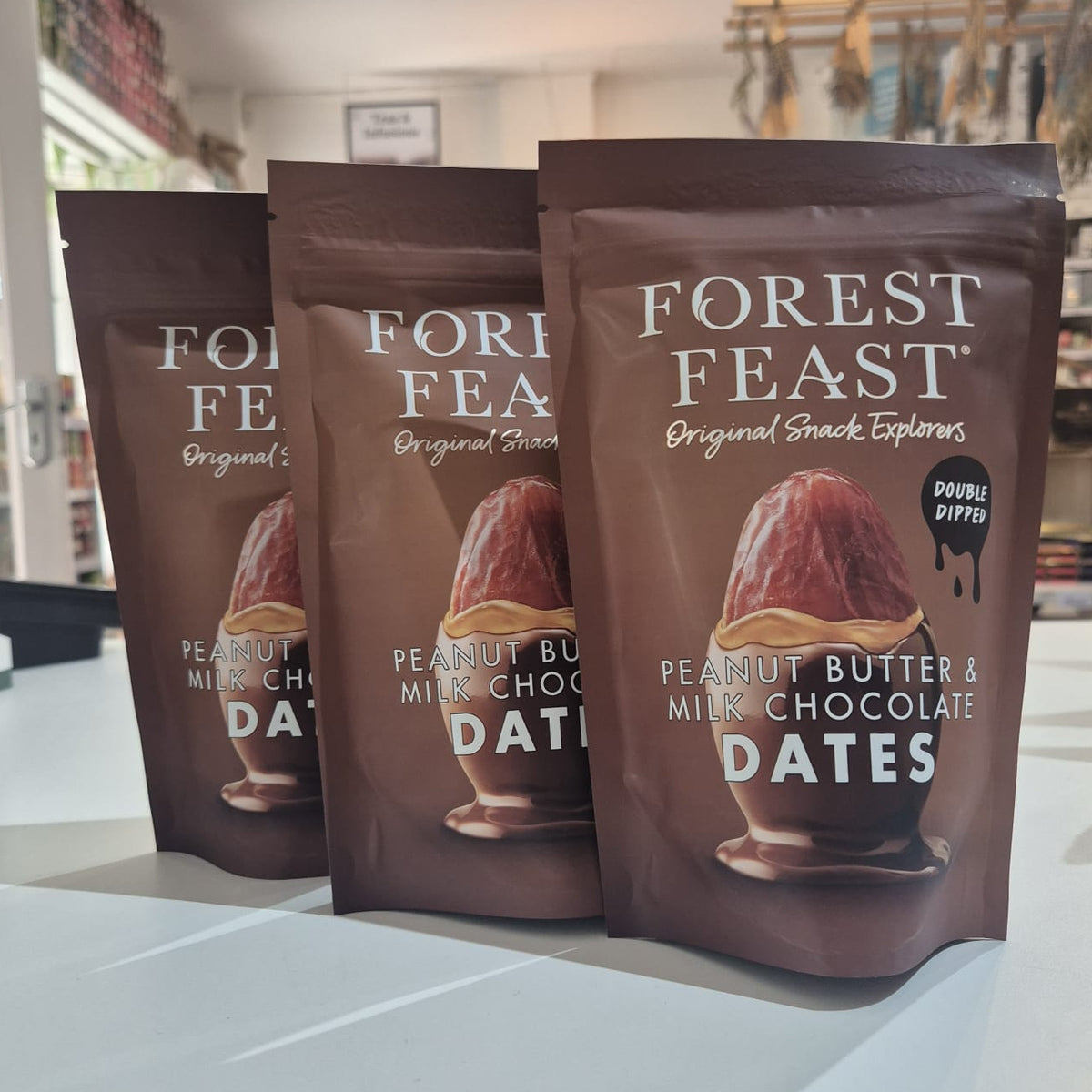 Three packages of Forest Feast peanut butter and milk chocolate dates on a white surface.