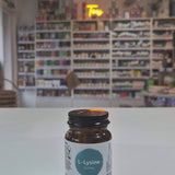 Supplement bottle labeled 'Viridian L-Lysine' on a white surface with a blurred background of shelves.