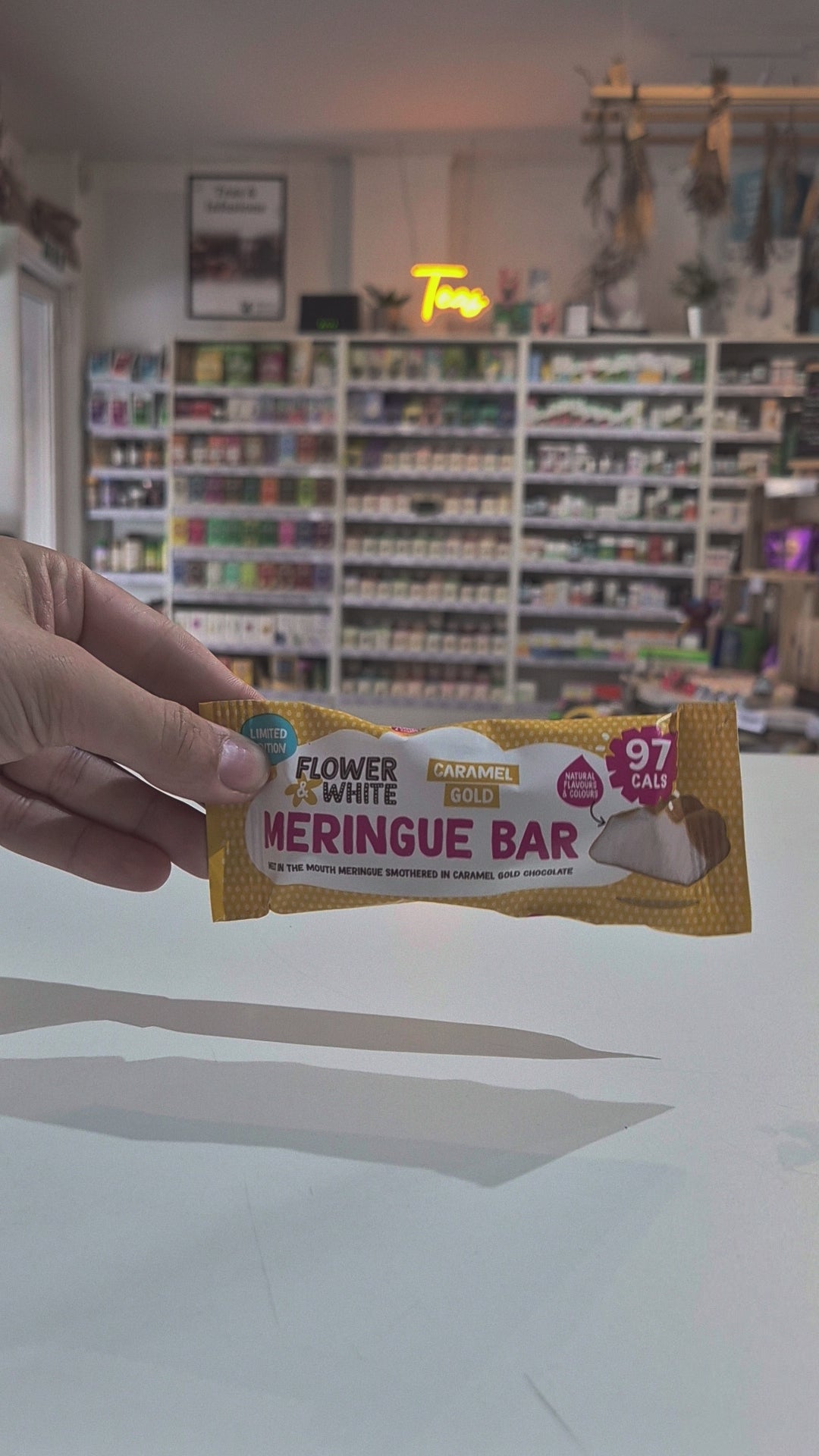 A packaged meringue bar snack placed on a white counter in a blurred shop interior with shelves and hanging decor in the background video
