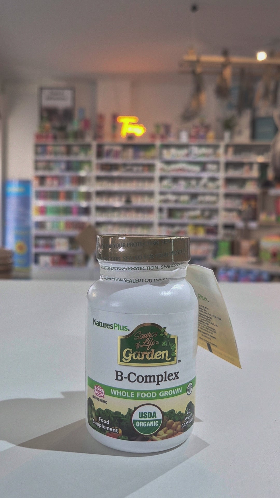 Nature's Plus B-Complex supplement bottle on a white surface with blurred store background video