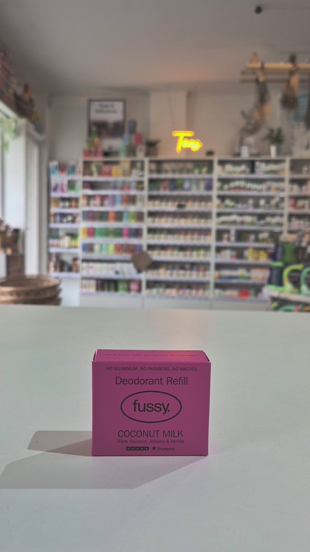 Pink deodorant refill box labeled 'fussy' on a counter with a store background.