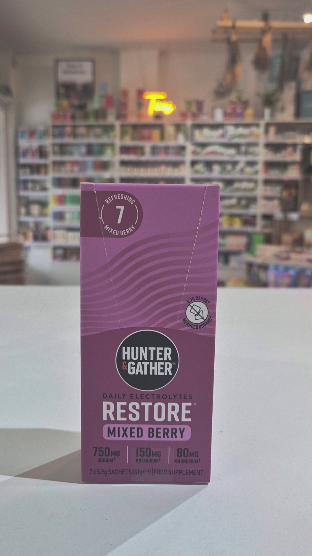 Purple box of Hunter & Gather Restore Mixed Berry electrolytes with a blurred store interior in the background