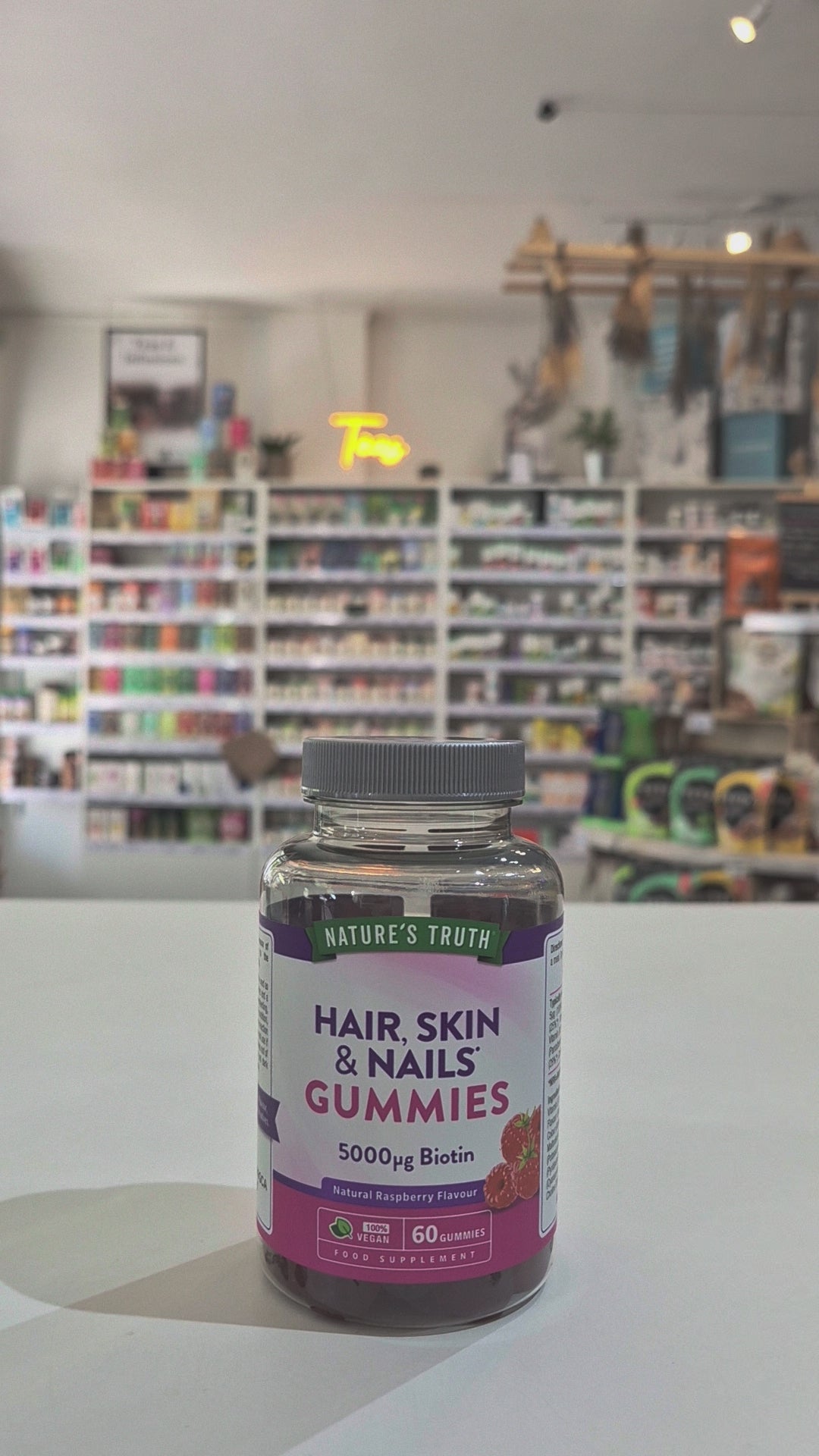 Nature's Truth Hair, Skin & Nails Gummies bottle on a white surface with a blurred store background video