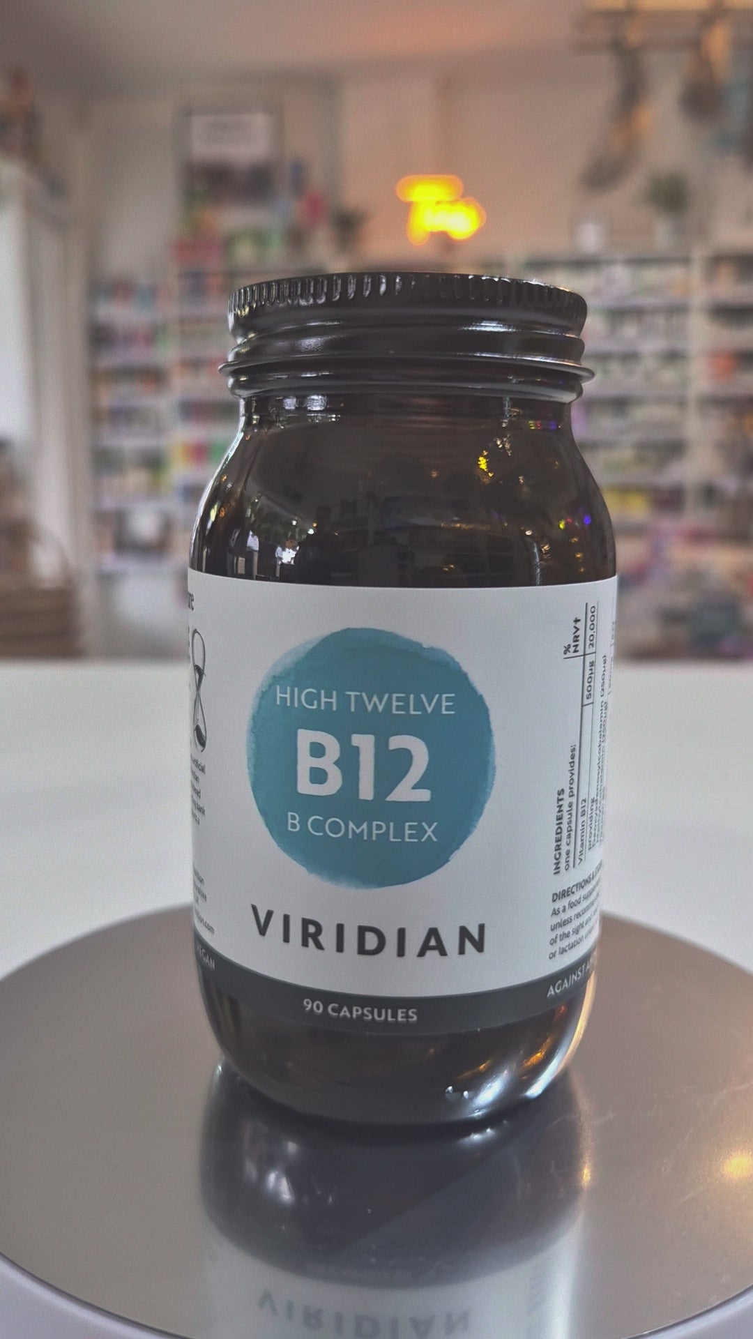 Jar of Viridian High Twelve B12 B Complex supplement on a white surface with a blurred store background video. 