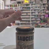 A glass jar of Saucerer Wild Mushroom Truffle Oil pesto with a black lid and brown label, sitting on a white table in a blurred shop interior Video