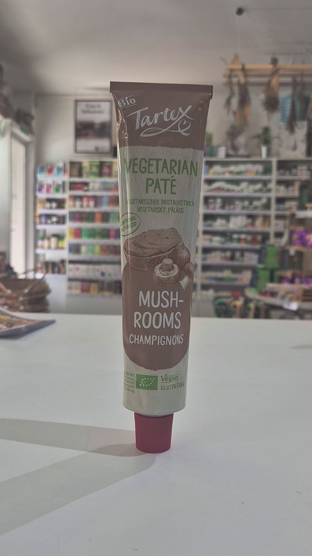 A tube of Tartex Vegetarian Pate Mushrooms on a white countertop with a blurred grocery store background.