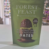 Green package of Forest Feast pistachio crisp milk chocolate dates on a white surface with a store background.