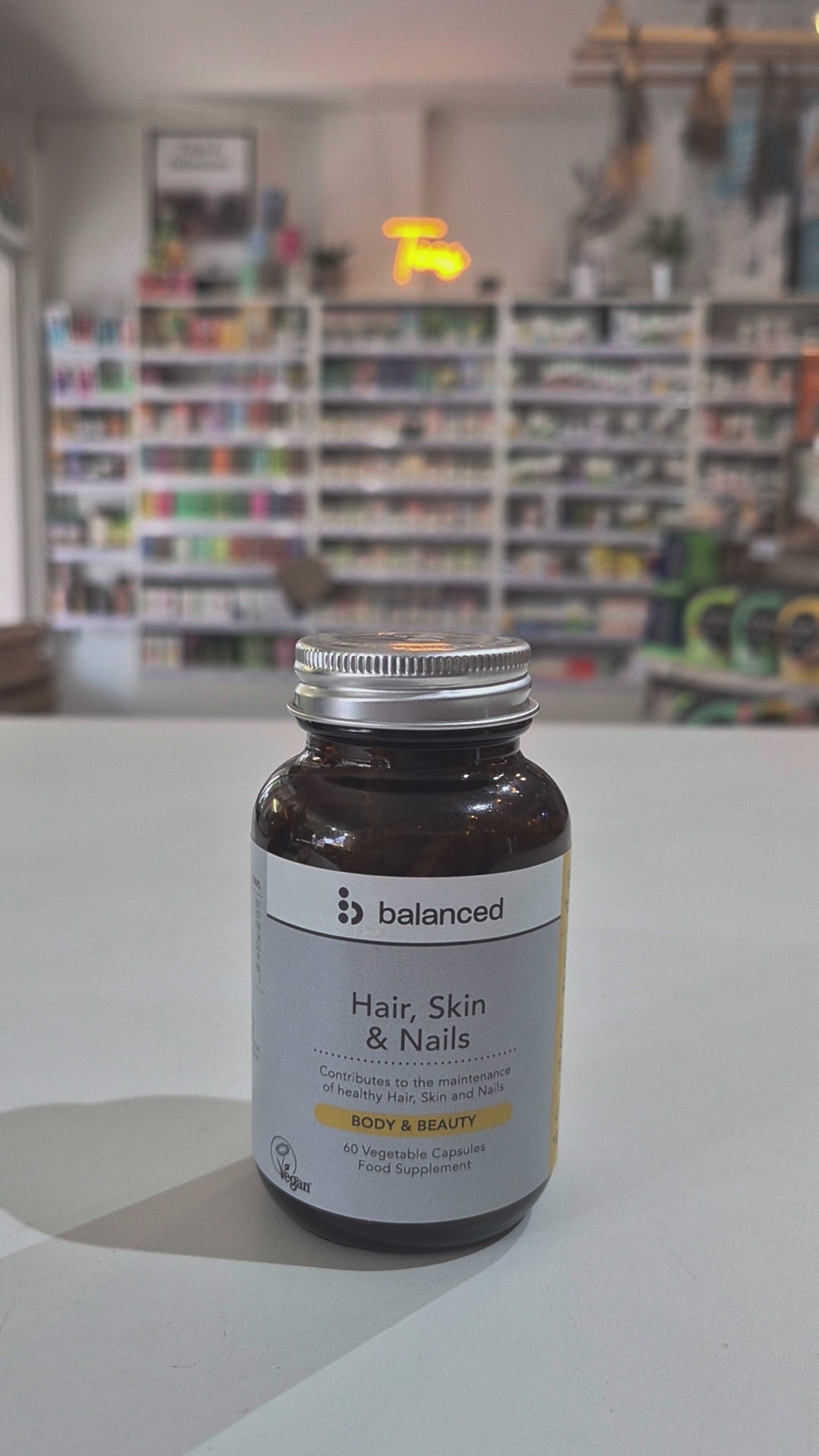 Supplement bottle labeled 'balanced' for hair, skin, and nails on a table with a blurred store background video