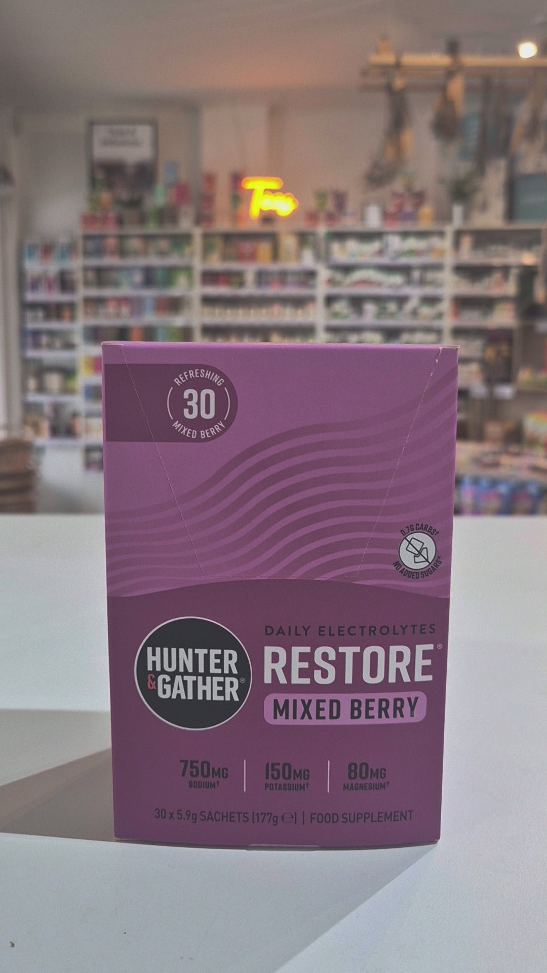 Purple Hunter & Gather supplement package with 'Restore' and 'Mixed Berry' text on a blurred indoor background. 