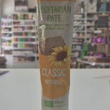 A tube of Tartex Vegetarian Pate Classic spread, featuring a yellow and white label with a sunflower graphic, lying on a white surface with a blurred store background.