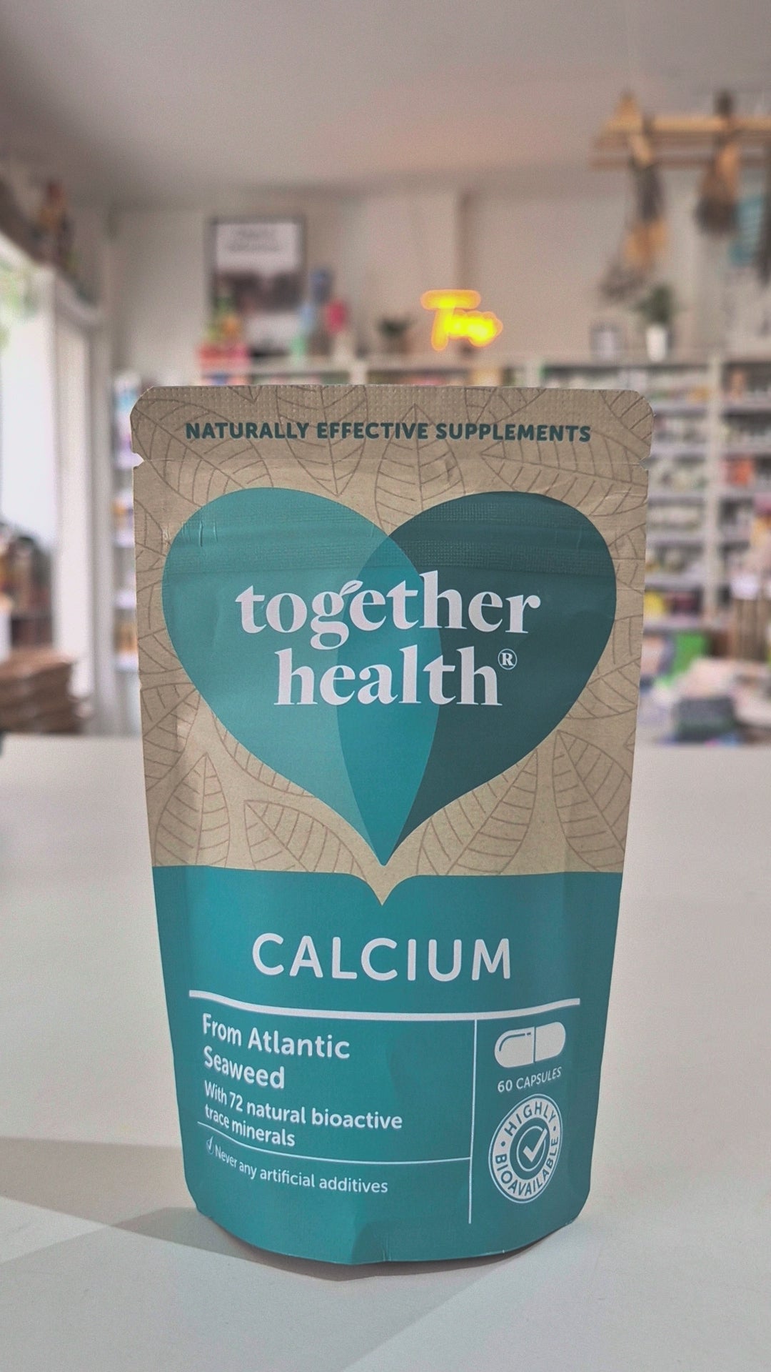 Packaging of Together Health Calcium supplements with a clear window showing the tablets inside. The package is predominantly blue and white with a heart shape design in a shop setting video. 