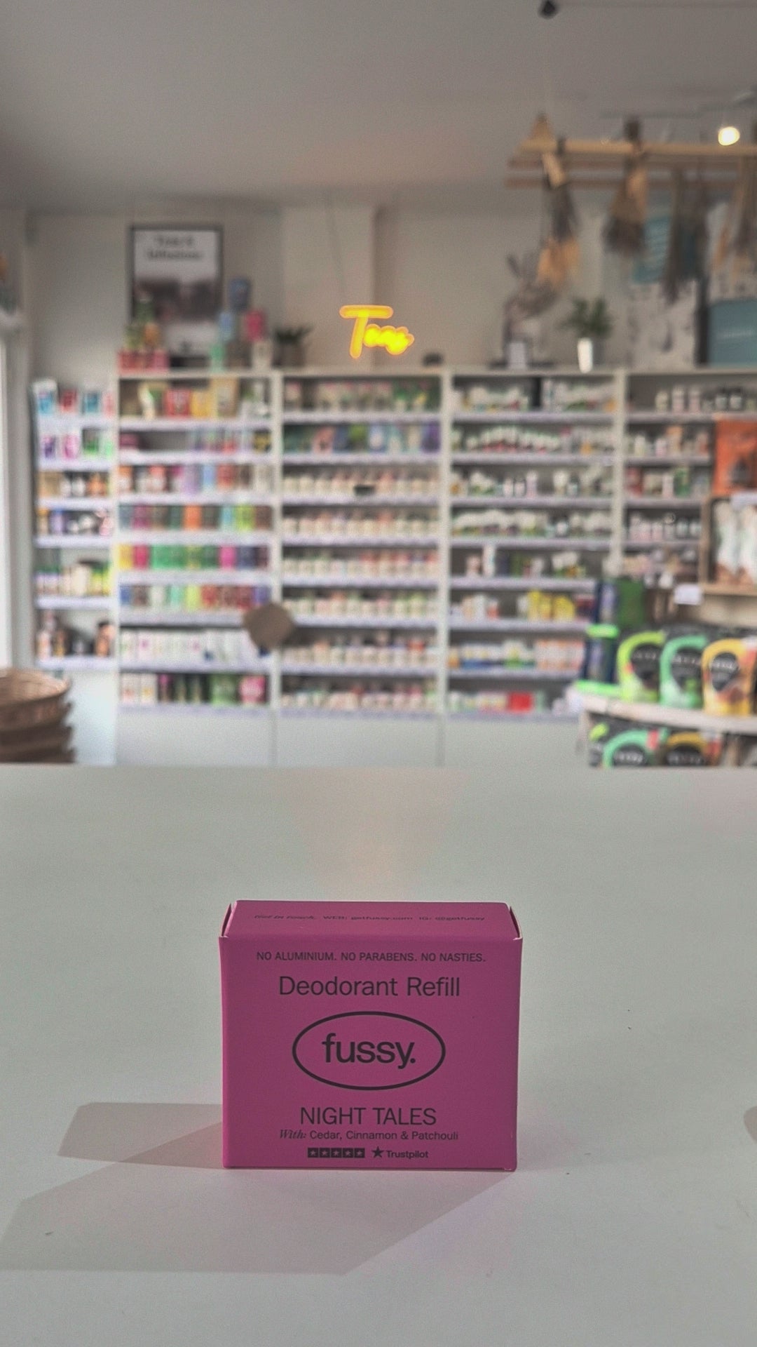 Pink deodorant refill box labeled 'fussy' on a gray surface with a blurred store background.