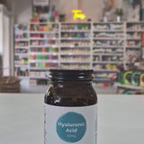 Brown supplement bottle labeled 'Hyaluronic Acid' by Viridian on a white surface with a blurred store background.