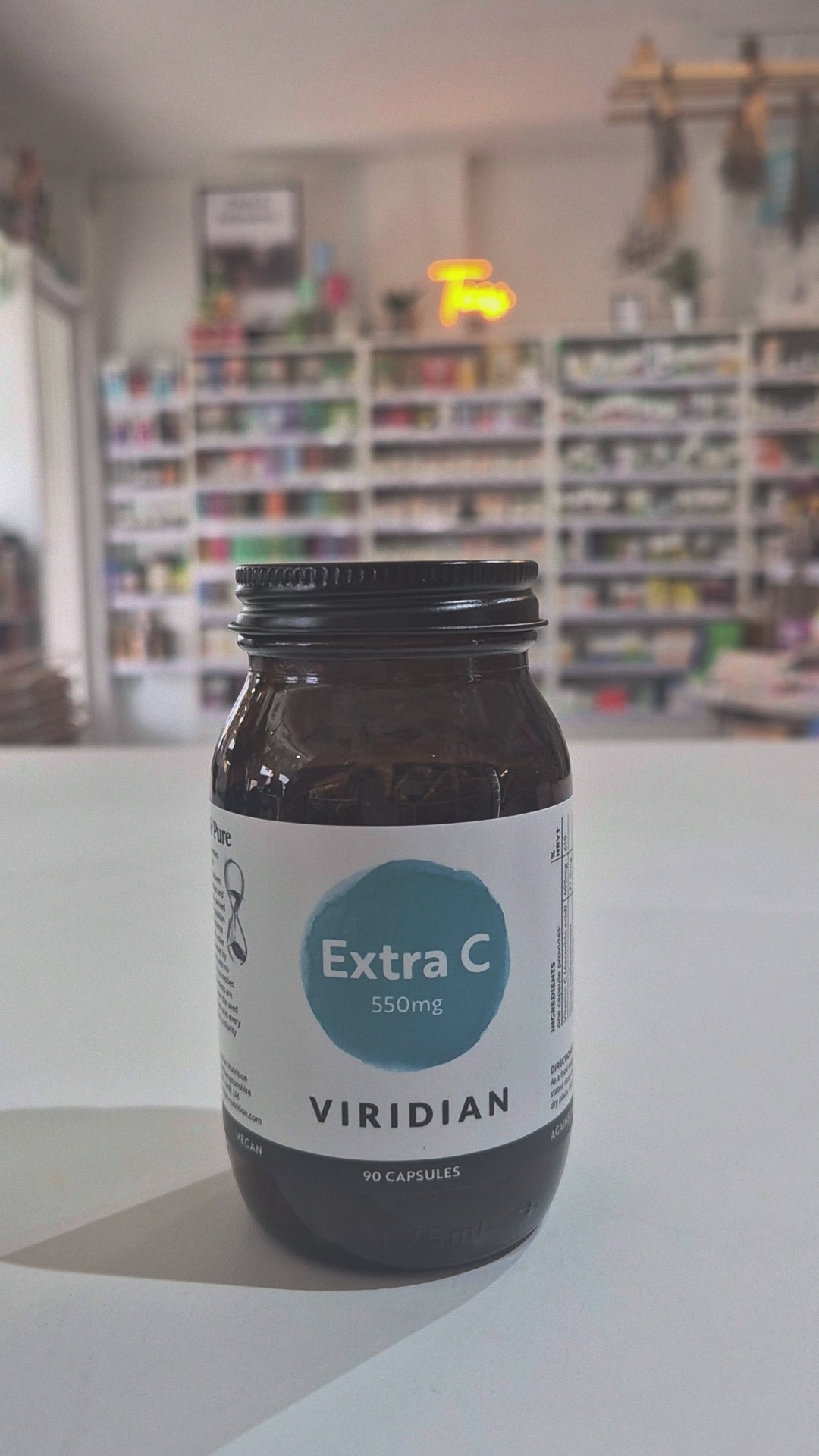 Brown supplement bottle labeled 'Extra C 550mg' by Viridian on a white surface with a blurred store background as a video