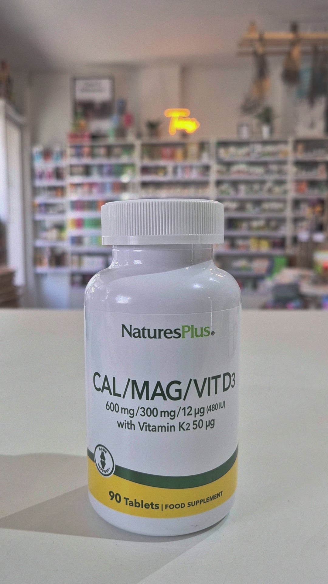 NaturesPlus Cal/Mag/Vit D3 supplement bottle on a table with a blurred store background video