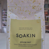 A pack of Soakin Epsom salt, with the branding visible on the front. The packaging is clear, allowing the reader to see the product inside, and it is labeled as '100% Pure Natural Salts' and 'RELAX & REVIVE Tired & Aching Muscles' as a video
