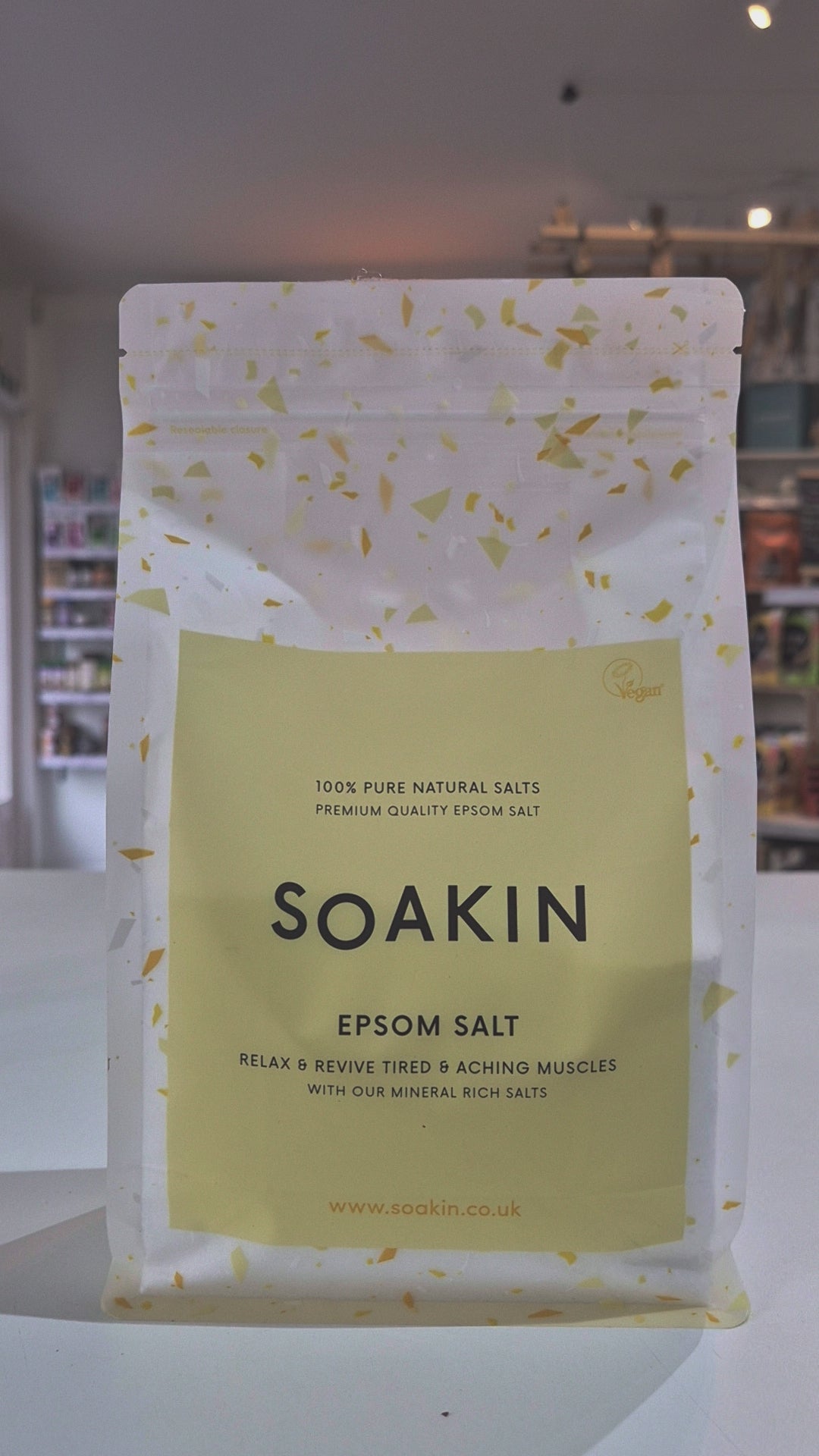 A pack of Soakin Epsom salt, with the branding visible on the front. The packaging is clear, allowing the reader to see the product inside, and it is labeled as '100% Pure Natural Salts' and 'RELAX & REVIVE Tired & Aching Muscles' as a video