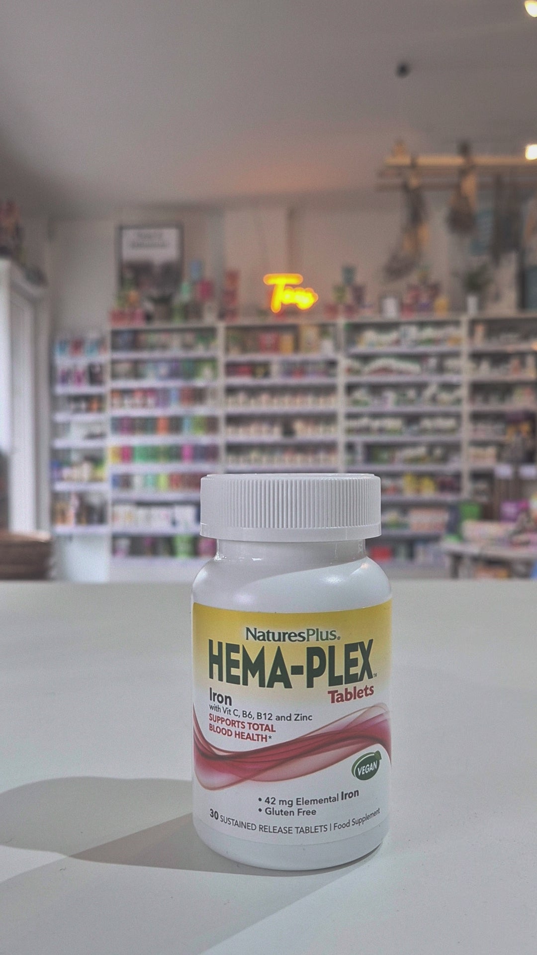 Bottle of Natures Plus Hema-Plex Tablets 42mg Elemental Iron, 30 capsules on a white surface with a blurred indoor background.