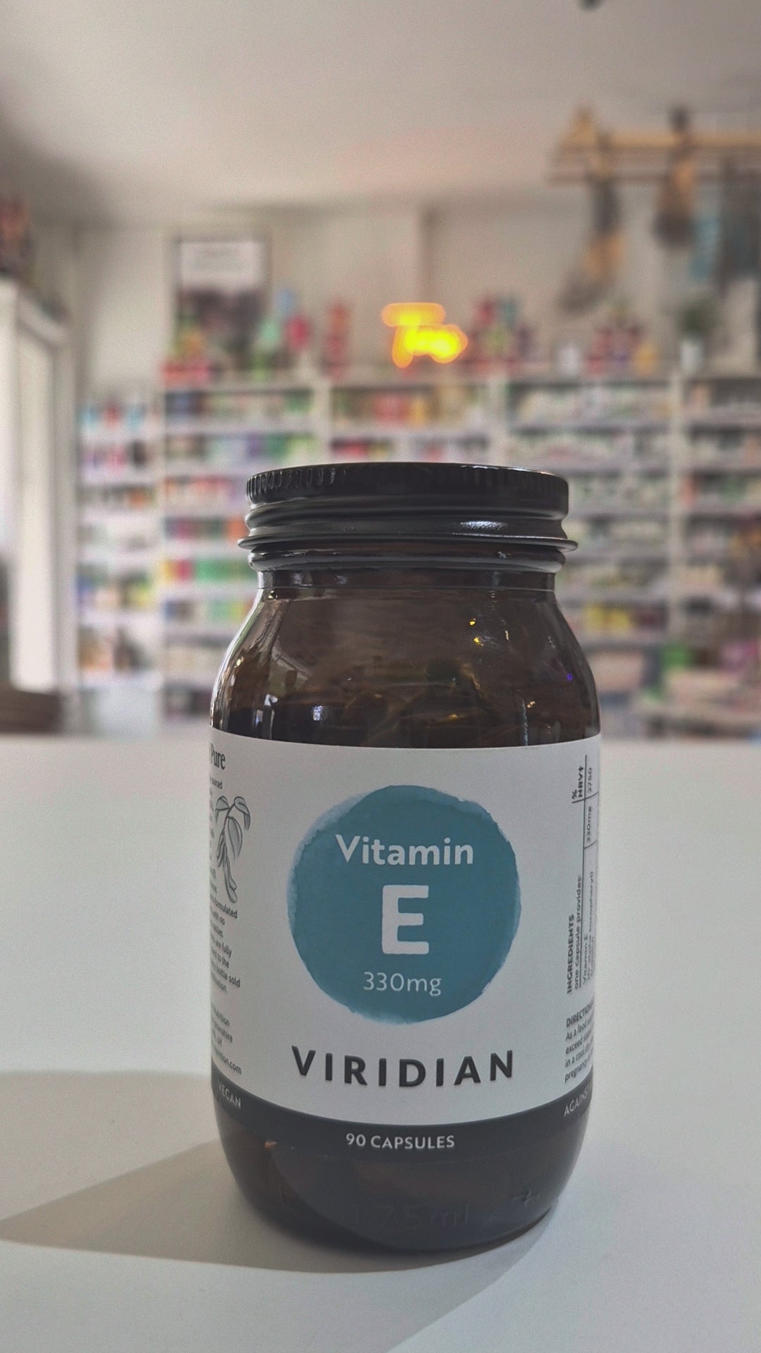 Jar of Viridian Vitamin E capsules on a white surface with a blurred store background
