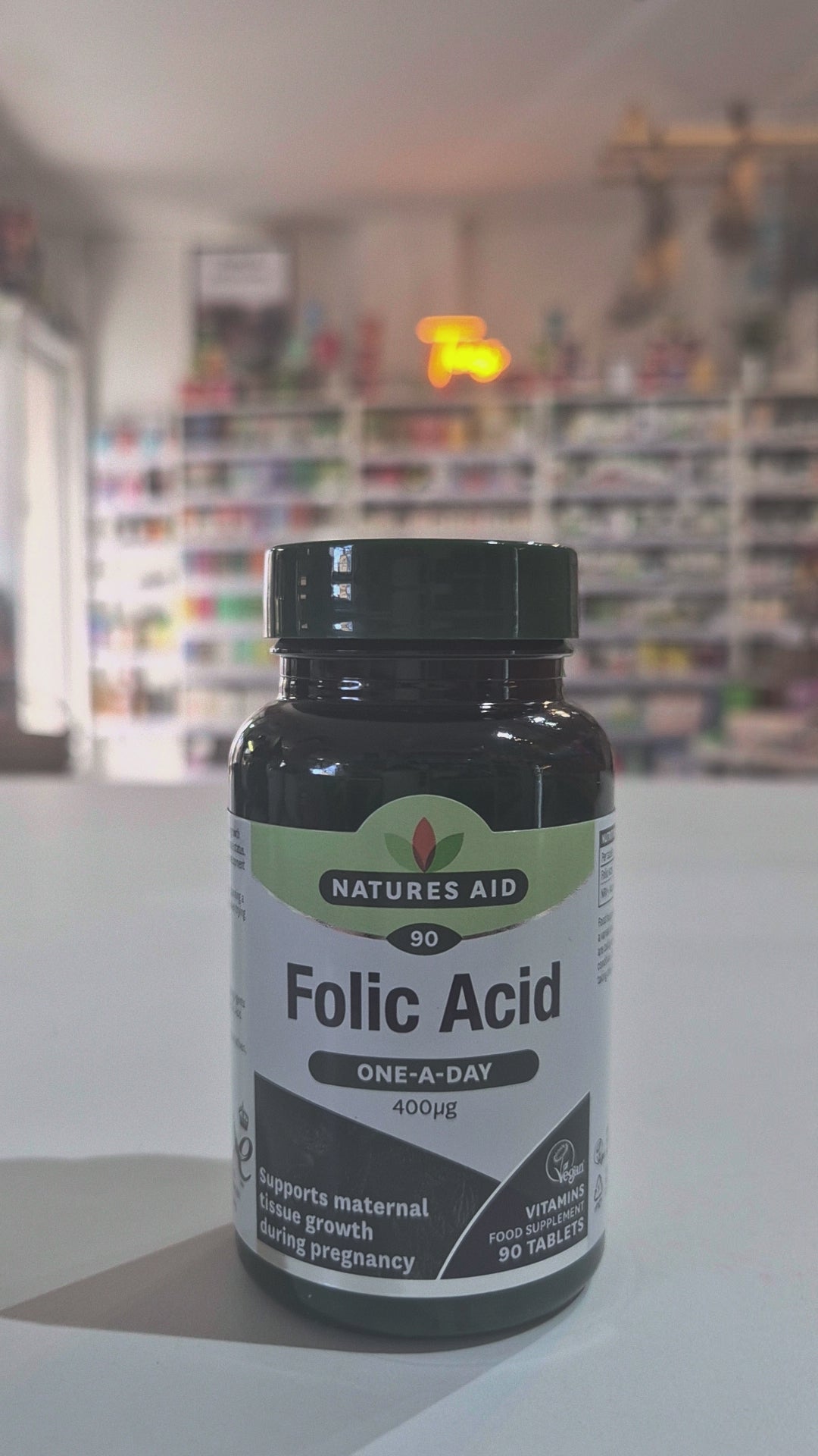 A bottle of Natures Aid Folic Acid supplement with 90 tablets, each providing 400 µg of folic acid. The label indicates the product supports maternal tissue growth during pregnancy and is vegan friendly.