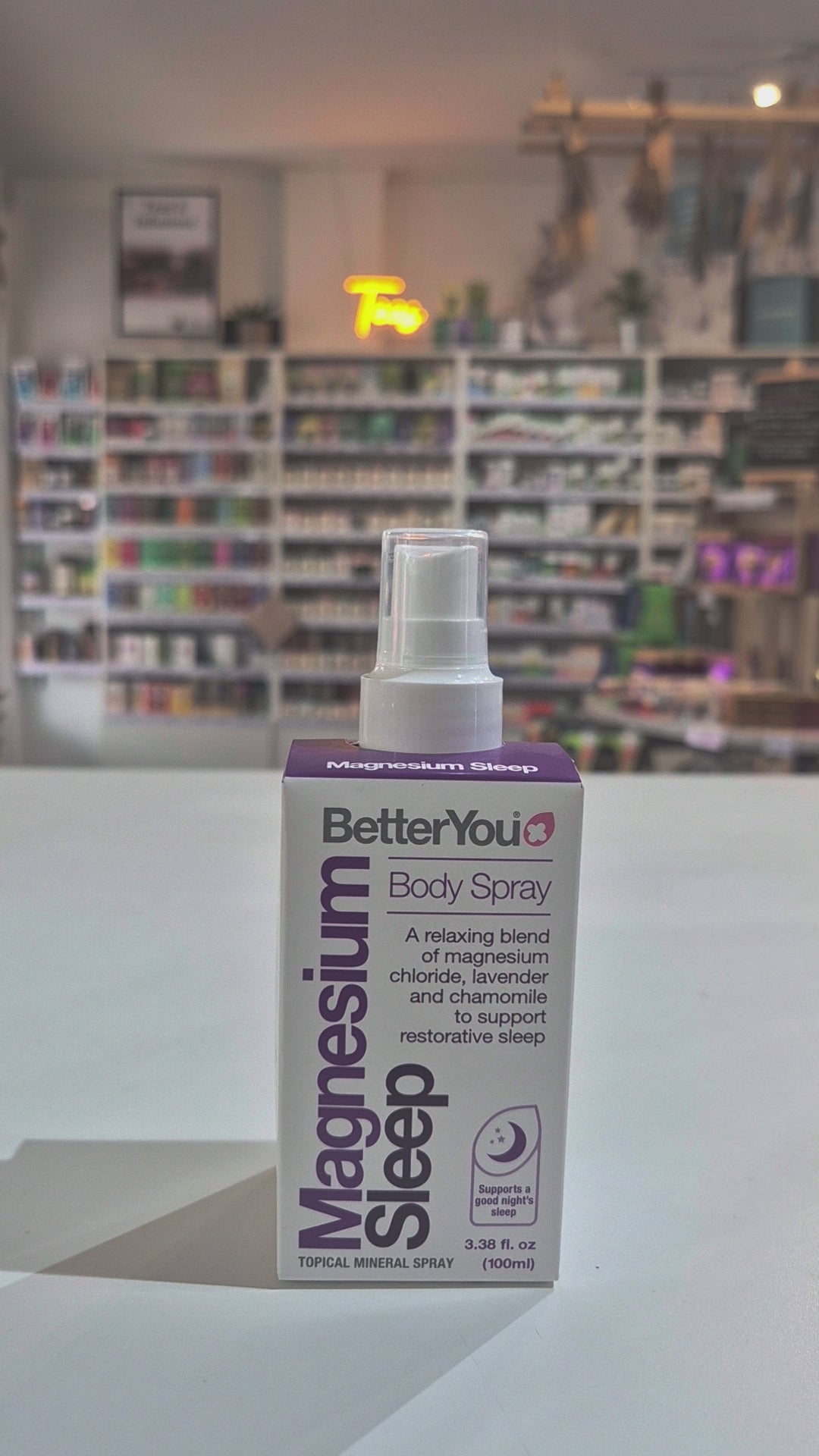 BetterYou Magnesium Sleep body spray bottle on a white surface with a store shelf in the background.