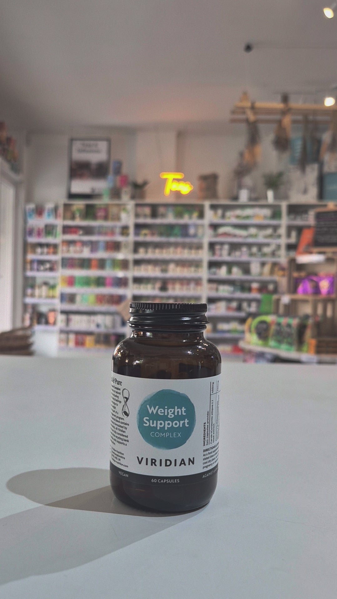 Brown supplement bottle labeled 'Weight Support Complex' by Viridian in a shop background. 