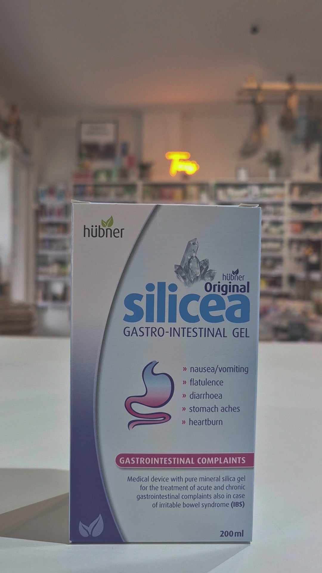 Packaging of Hubner Original Silicea Gi Gel 200Ml for gastro-intestinal complaints, displaying indications such as nausea, vomiting, flatulence, diarrhoea, stomach aches, and heartburn in a shop, on a counter video