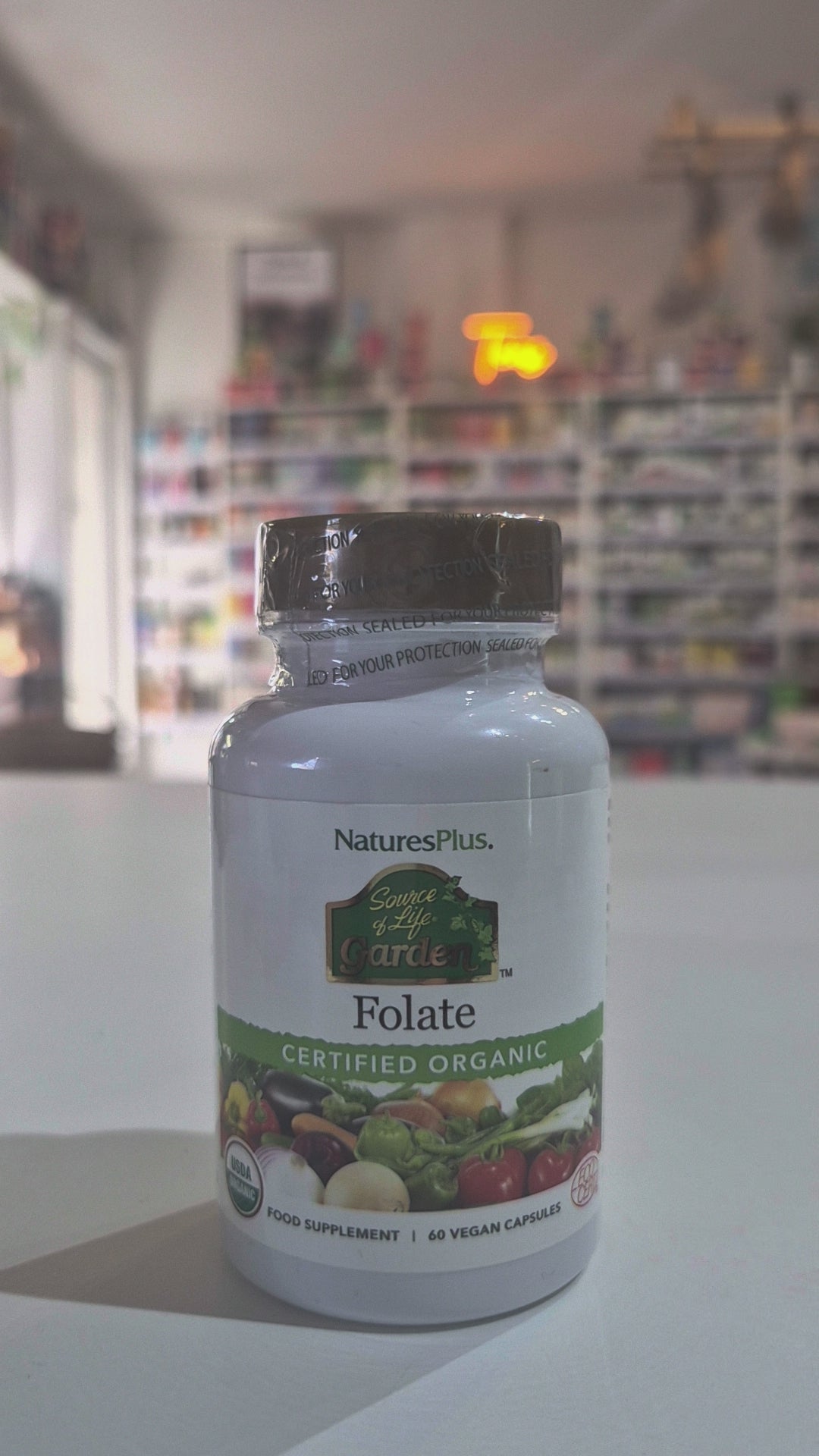NaturesPlus Folate supplement bottle on a Video in a shop background