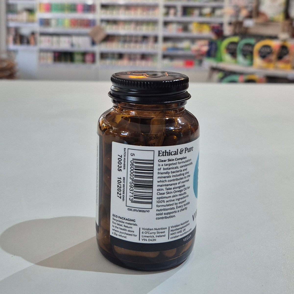 Amber glass bottle with a label on a white surface, blurred store shelves in the background