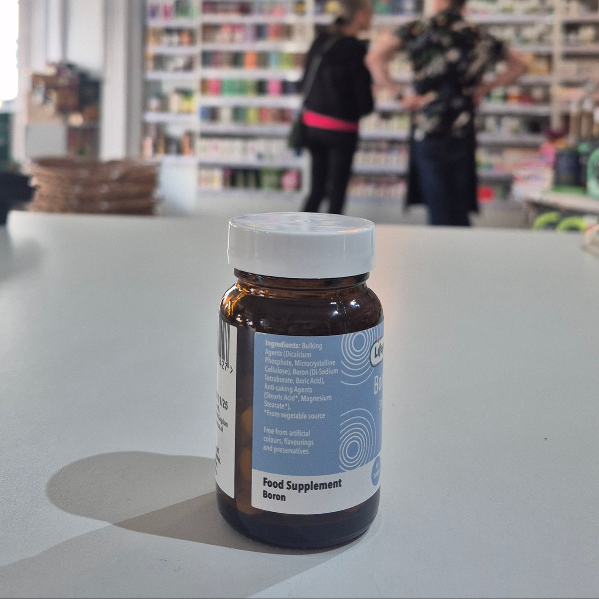 Supplement bottle on a counter with blurred people and shelves in the background
