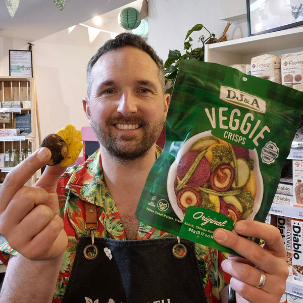 Green package of DJ&A Veggie Crisps with a bowl of colourful vegetables on a white background.