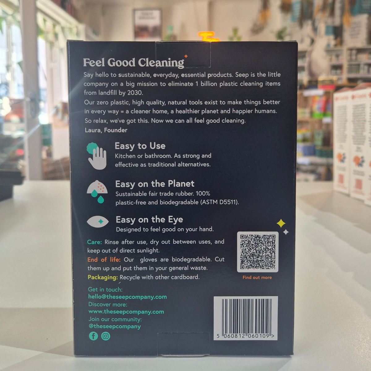 Back cover of a pack of large rubber gloves with text and QR code on a blurred indoor background
