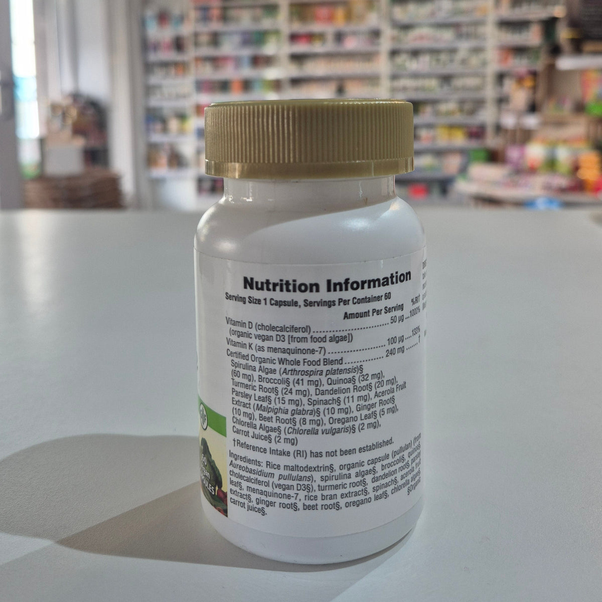 Close-up of a supplement bottle with nutrition information label, blurred store interior in the background