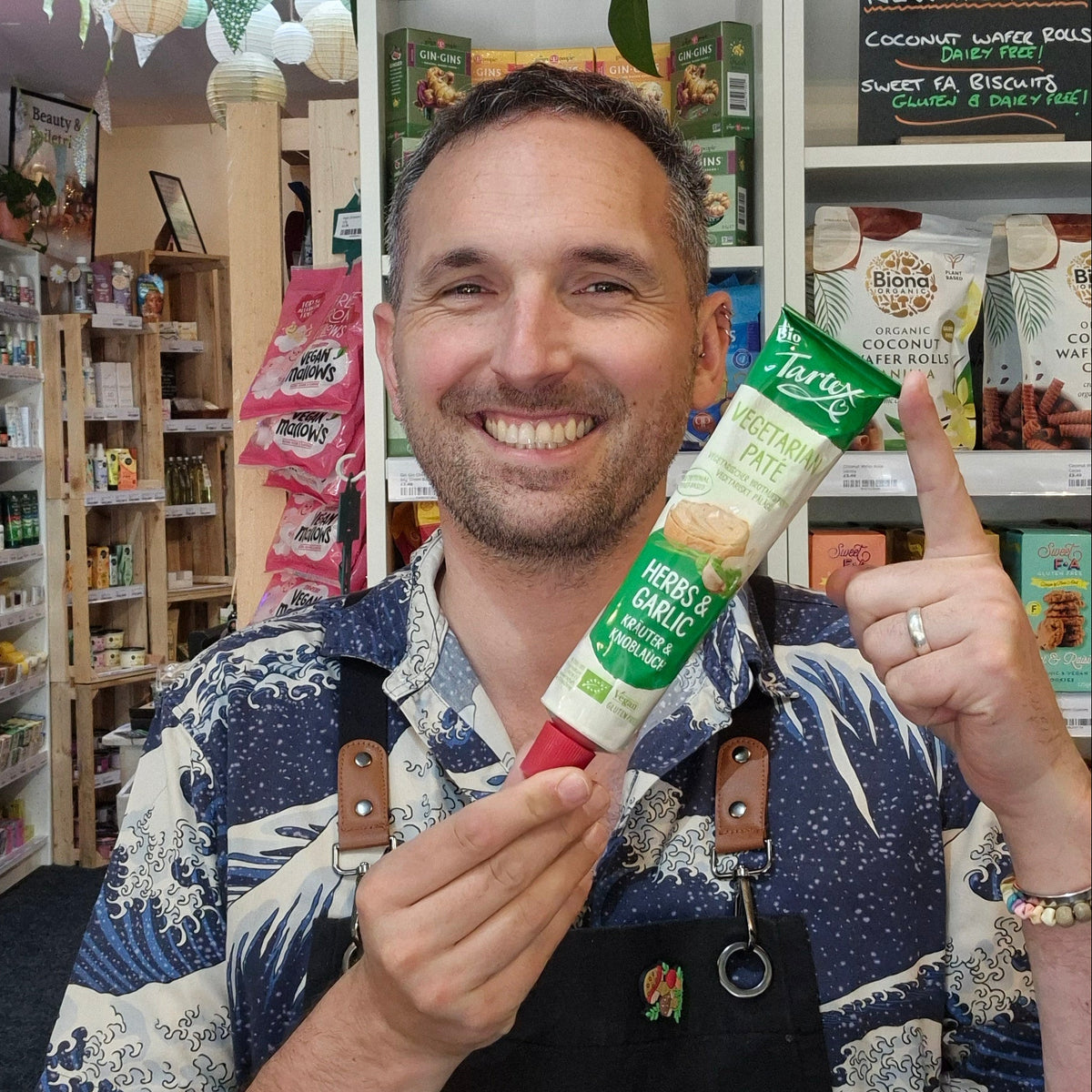 A Smiling man holding a squeeze tube Tartex Herbs and Garlic with a pink cap. 