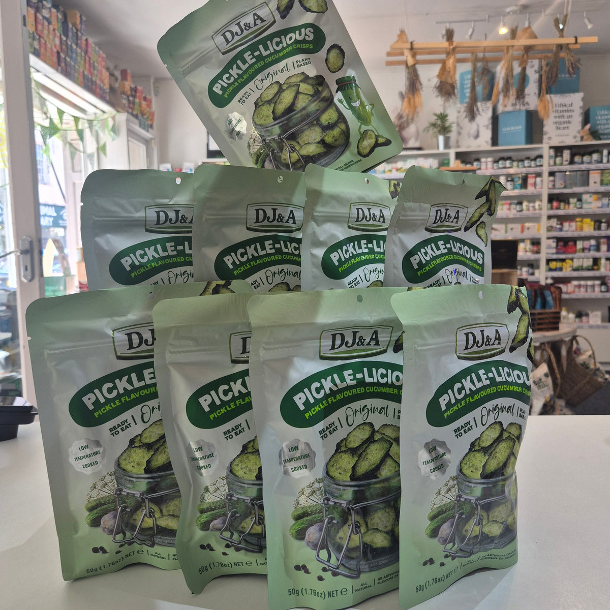 Multiple packages of DJ&A's Pickle-Licious Pickles on a white surface with a blurred store background.