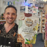 Man holding a package of Biona Organic Coconut Wafer Rolls Vanilla in a store.