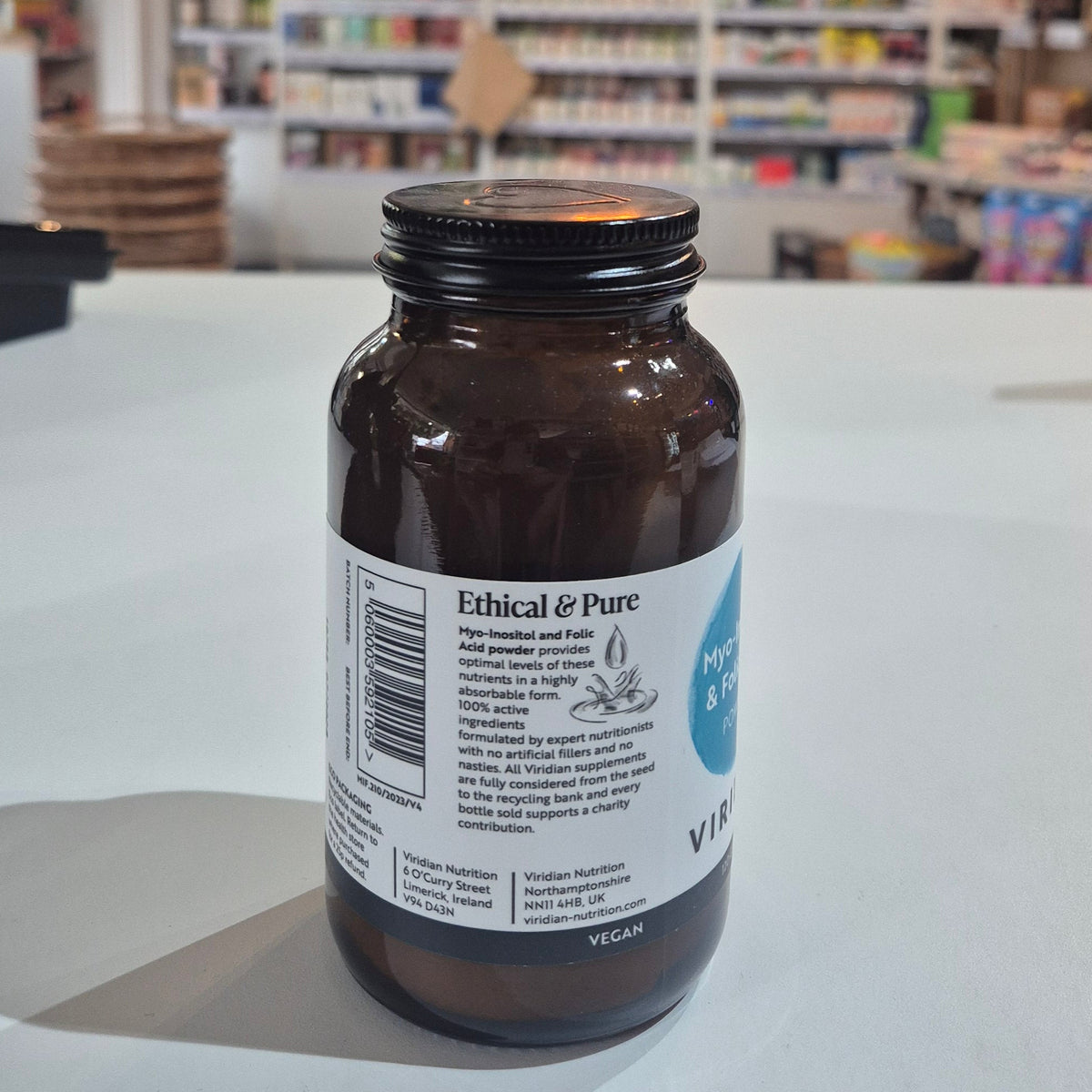 Myo-Inositol & Folic supplement bottle with Viridian label on a white surface, with  blurred store interior in the background