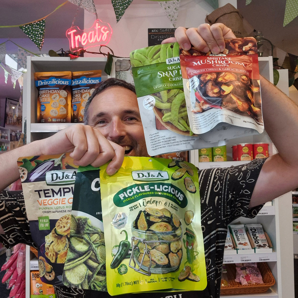A smiling man holds up five bags of DJ&A