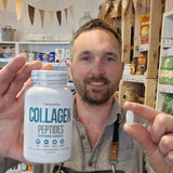 Man holding a bottle of NaturesPlus Collagen Peptides and a supplement capsule in a store setting.