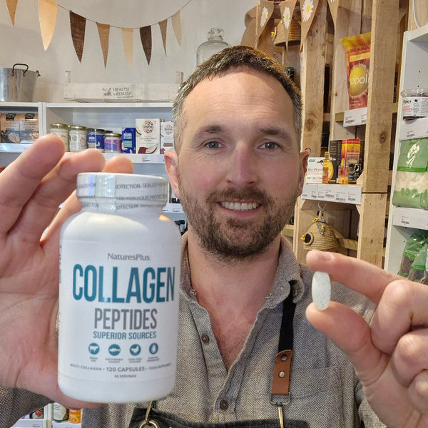 Man holding a bottle of NaturesPlus Collagen Peptides and a supplement capsule in a store setting.