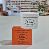 Fussy compostable deodorant refill container and packaging on a table with a blurred store background.