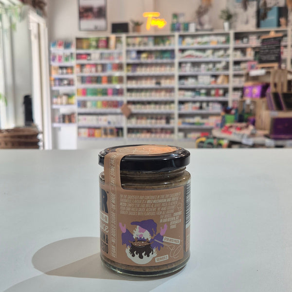 A glass jar of Saucerer Wild Mushroom Truffle Oil pesto with a black lid and brown label, sitting on a white table in a blurred shop interior.