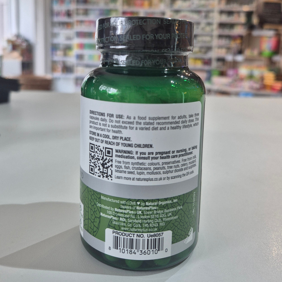 Green supplement bottle with label and QR code on a blurred store background