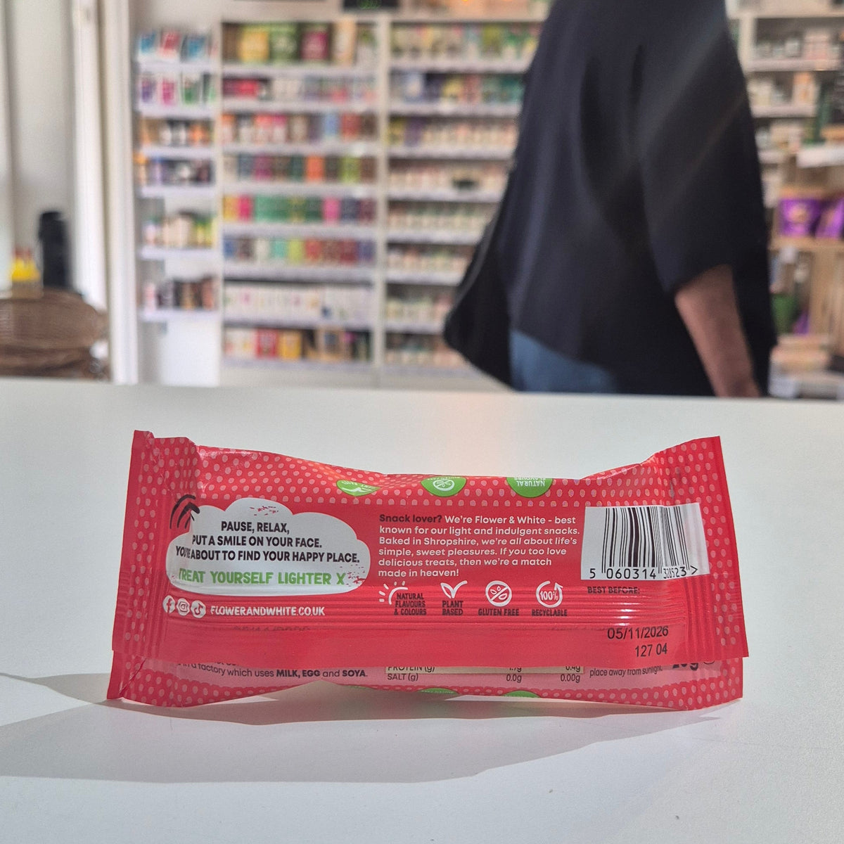 A packaged meringue bar in a red and white wrapper labeled 'Flower & White' and 'Chocolate Dipped Strawberry', placed on a white surface with a blurred store shelf background.