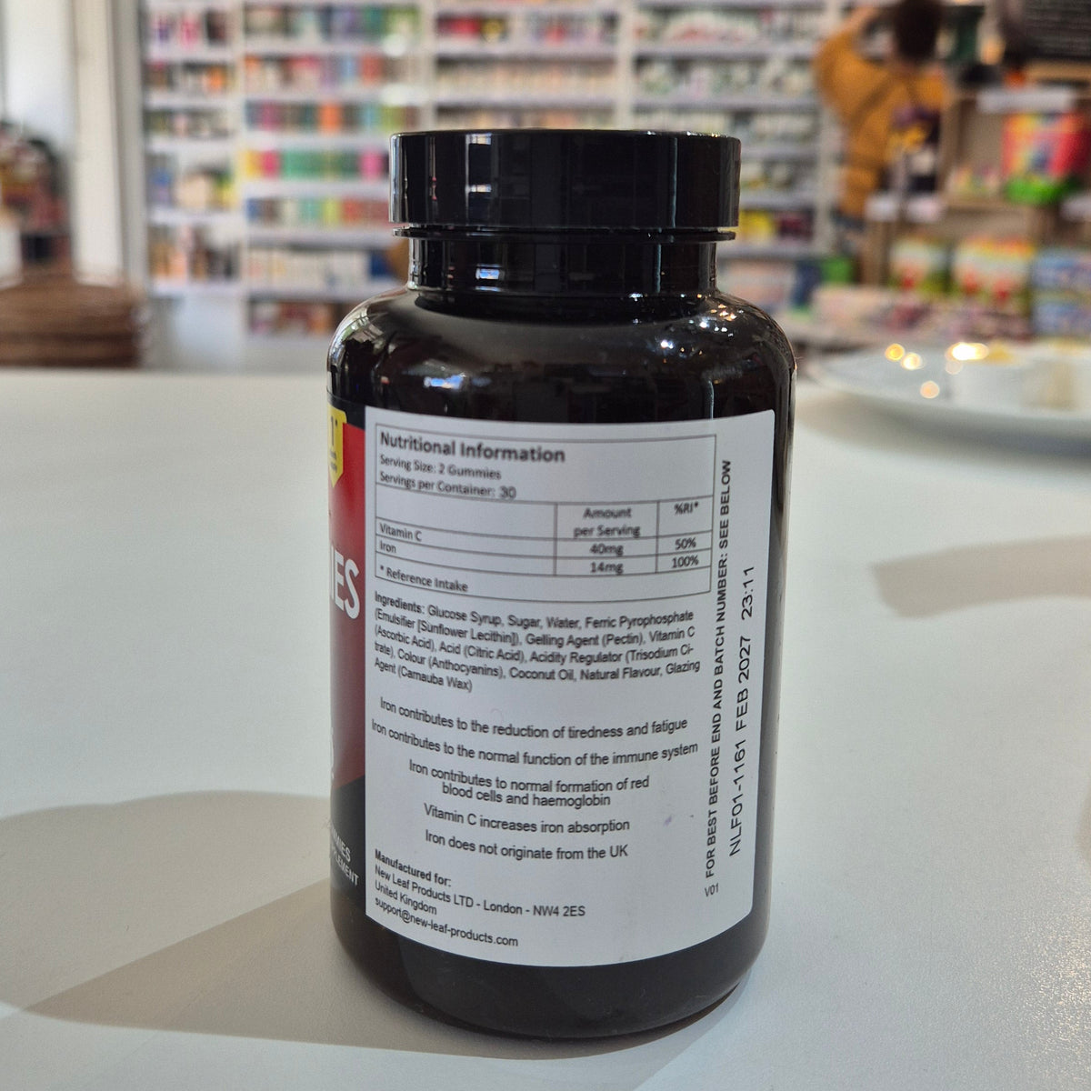 Black supplement bottle with nutritional label on a white surface, blurred store background