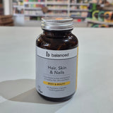 Supplement bottle labeled 'balanced' for hair, skin, and nails on a table with a blurred store background.
