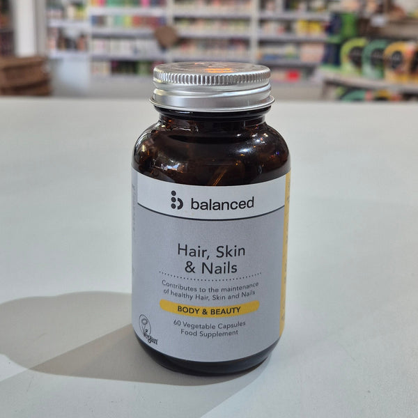 Supplement bottle labeled 'balanced' for hair, skin, and nails on a table with a blurred store background.