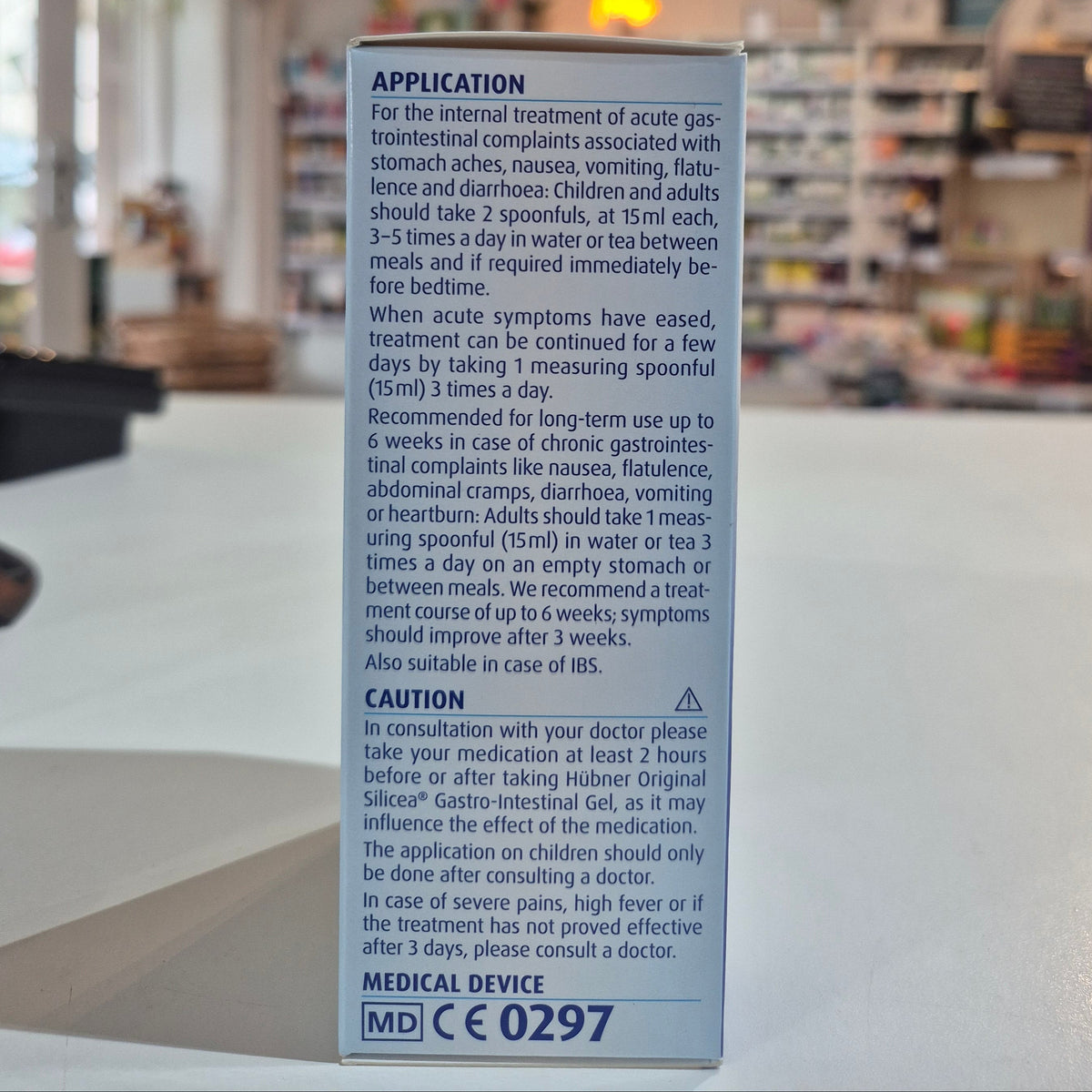Packaging of Hubner Original Silicea Gi Gel 200Ml for gastro-intestinal complaints, displaying indications such as nausea, vomiting, flatulence, diarrhoea, stomach aches, and heartburn in a shop, on a counter, application instructions. 